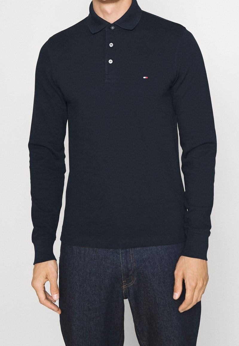 Camisa polo de manga larga en algodón azul marino con cuello abotonado, que presenta un pequeño logo en el pecho y un dobladillo recto.