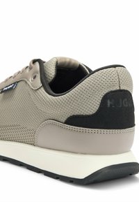Sneaker con una toma in rete beige, accento in suede nero e suola in crema ammortizzata. Include un design testurizzato lungo il corpo.