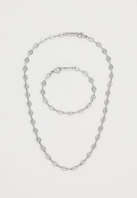 Hopeaketju ja rannekorusetti, joissa on ovaalit lenkit ja rapu-tyyppiset sulkijat. Minimalistinen muotoilu ja kiillotettu pinta.