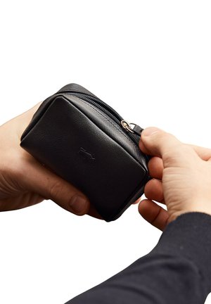 Piccola borsa nera in pelle con chiusura a zip, caratterizzata da una texture liscia e angoli arrotondati, tenuta tra due mani.