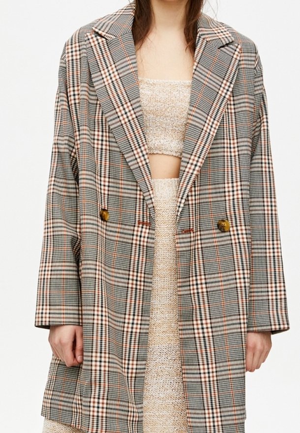 Dubbelknäppt rutigt yllekapp i grå, beige och orange nyanser, med breda slag, två framfickor och oversize-design med lös passform.