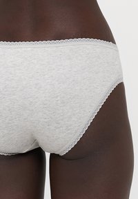 Grijs katoenen slip met een kantafwerking langs de tailleband. De stof lijkt zacht en heeft een subtiele gemêleerde textuur.