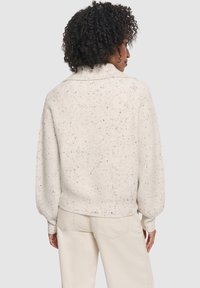 Maglione a maglia di colore crema con una texture a coste, dalla vestibilità morbida e spalle scese. Presenta delle macchie multicolori in tutto il capo e un colletto corto.
