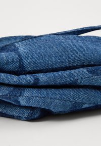 Tessuto di denim piegato con tonalità di blu a contrasto, che presenta un delicato motivo testurizzato e dettagli di cucitura visibili.