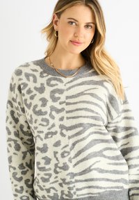 Grey and cream sweater with animal print design, featuring a round neckline, long sleeves, and ribbed cuffs. Soft texture with prominent patterns.