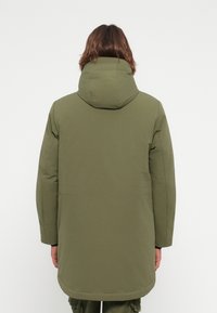 Pufferjack in olijfgroen, met een capuchon, lange mouwen en een rechte snit met naadloze, gewatteerde textuur.