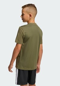 Olivovo zelené krátke športové tričko s okrúhlym výstrihom, v kombinácii s čiernymi šortkami s bielymi bočnými pruhmi. Texturovaná látka.