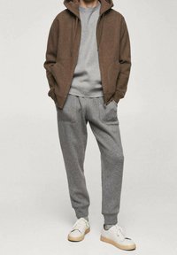 Hoodie zippé marron, t-shirt gris et pantalon de survêtement gris avec poches ; assortis à des baskets blanches ; matériaux doux et texturés, coupe décontractée.