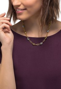 Gold and silver chain necklace featuring oval links with circular accents, worn over a purple top, showcasing a layered design.