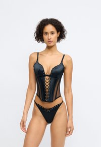 Schwarzes Dessous-Set bestehend aus einem Satin-Corsette mit Schnürung vorne, Unterwäschen mit Drahtbügeln und Netzpaneelen, kombiniert mit einem passenden Tanga.