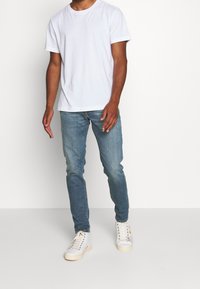 T-shirt blanc en coton à manches courtes, associé à un jean en denim bleu clair. Chaussures : baskets montantes blanches avec semelles de couleur fauve.