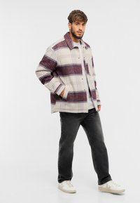 Sacou în carouri de culoare crem și burgundy, cu guler, închis cu butoane și buzunare laterale; asortat cu blugi negri și teneși albi.