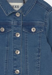 Chaqueta de mezclilla en azul medio, con cuello, dos bolsillos en el pecho y botones a presión plateados en el frente para el cierre.