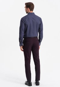 Camisa azul marino a rayas con cuello extendido, mangas largas y botones blancos, combinada con pantalones marones ajustados y zapatos negros.