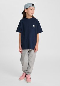 Marinblå bomullströja med korta ärmar, grå sweatpants och rosa sneakers; keps med en logotyp i ljusblått och med platt skärm.