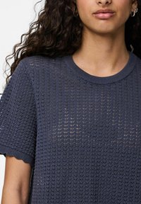 Pletený svetr námořnické modré barvy s volným střihem, texturovaným vzorem, ribovaným kulatým výstřihem a vlnitými zakončeními rukávů. Lehký a poloprůhledný.