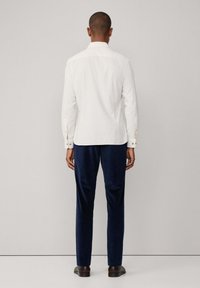Witte longsleeve overhemd met knoopmanchetten, gecombineerd met marineblauwe broek. Het overhemd heeft een standaard kraag en een gladde textuur.