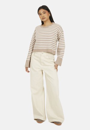 Gestreepte cropped trui in beige en crème, gecombineerd met wijde off-white broeken. Zachte textuur, ribbelig zoom en mouwen. Grijze schoenen.