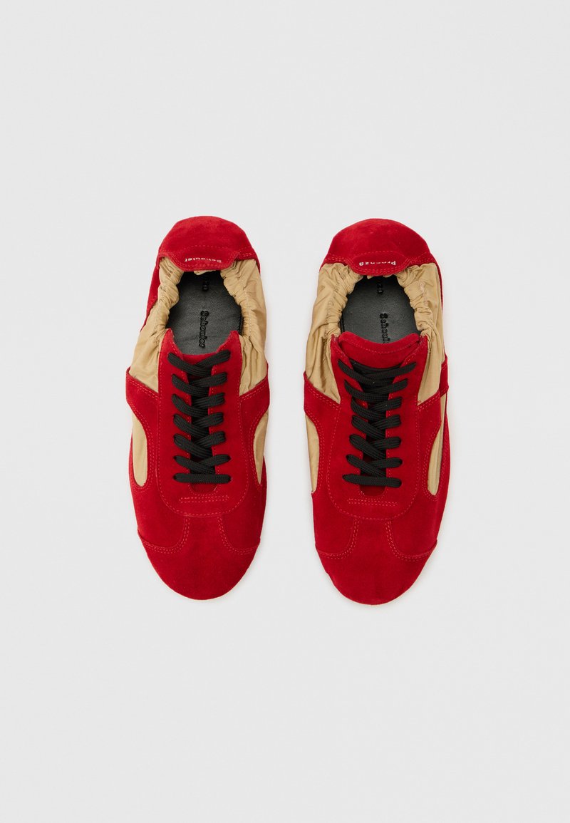 Par de zapatos casuales rojos y beige con cordones negros y detalles elásticos alrededor del tobillo, vistos desde arriba sobre un fondo claro.