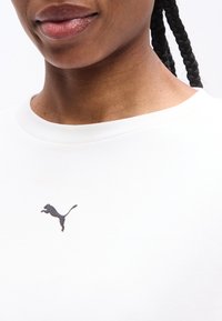 Gros plan sur une personne aux cheveux tressés portant un t-shirt blanc Puma avec le logo Puma visible sous l'encolure.