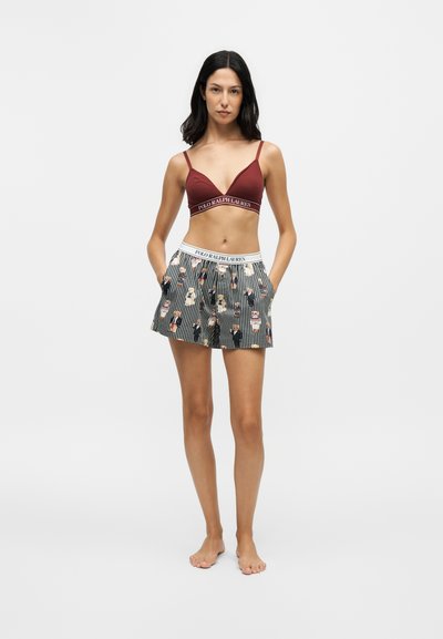 Femme debout pieds nus portant un bralette bordeaux et un short rayé avec une taille ornée d'un ours de dessin animé et du logo Polo Ralph Lauren.