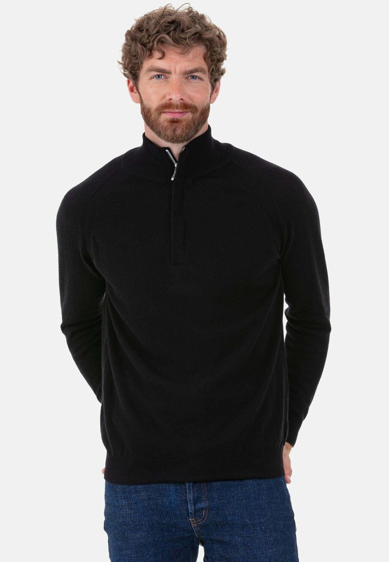 Schwarzer Strickpullover mit Reißverschluss am Hals aus weichem Stoff. Verfügt über einen hohen Kragen und gerippte Bündchen. Wird über blauen Jeans getragen und hat eine taillierte Passform.