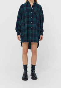 Fleeceklänning i mörk marinblå med grön och röd rutmönster, med krage, knäppning fram och en ficka på vänster bröst.