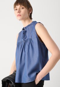 Μπλούζα χωρίς μανίκια σε μπλε χρώμα με ριχτό λαιμό, συγκεντρωμένο ύφασμα κάτω από το στήθος και λεπτομέρεια με κορδόνι. Μαλακό, ελαφρύ υλικό.