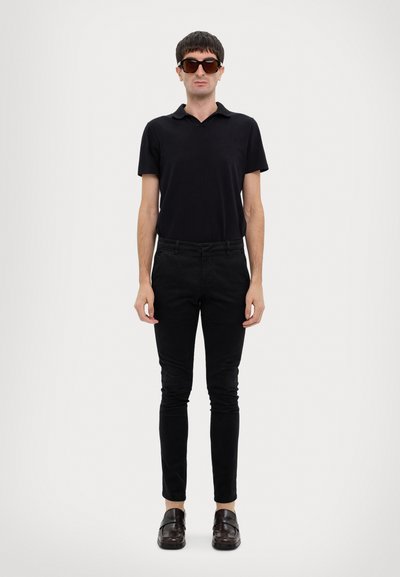 Polaire noir, pantalon slim noir, mocassins marron et lunettes de soleil surdimensionnées. Design simple, couleurs unies et détails matériels minimaux.