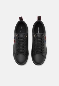 Black sneakers with a smooth synthetic upper, round toe, flat laces, and gold eyelets. Includes logo details and a textured side panel.