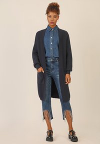 Granatowy prążkowany kardigan, jasnoniebieska koszula z guzikami w kropki, zniszczone dżinsy z frędzlami u dołu oraz czarne buty na platformie.