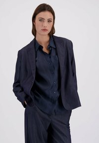 Mörkblå skräddarsydd blazer och skjorta; slät tyg med knäppning, avslappnad passform och strukturerad design. Inga mönster eller detaljer.