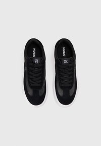 Black sneakers with a combination of suede and mesh material, featuring a white rubber sole, round laces, and a logo on the tongue.