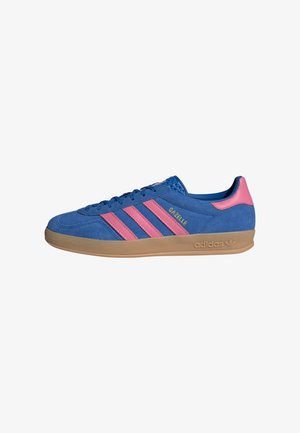 Niebieski zamszowy sneaker Adidas Gazelle z różowymi paskami, różową zakładką na pięcie i gumową podeszwą na białym tle.