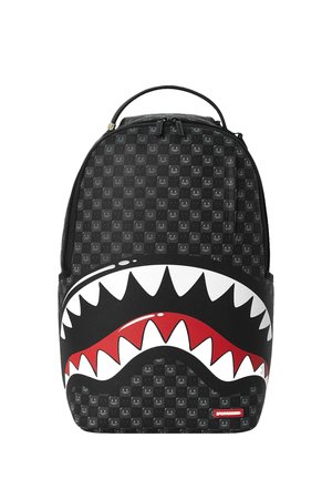Mochila negra con pequeño patrón de caras sonrientes grises y gran gráfico de boca de tiburón blanco y rojo en el bolsillo delantero.