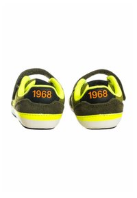 Un paio di sneaker nere e gialle per bambini con il testo arancione "1968" sul tallone, viste da dietro su uno sfondo bianco.