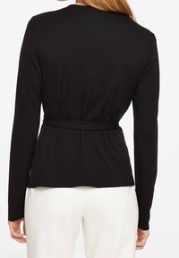 Zwarte lange mouwen top met een peplumdesign, nauwsluitende taille en zachte textuur, met een ronde halslijn en geen zichtbare sluitingen.