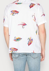 Koszula z krótkim rękawem w kolorze białym, ozdobiona kolorowymi nadrukami przynęt wędkarskich. Materiał jest gładki; koszula ma luźny fason i klasyczny kołnierzyk.