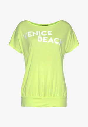 Top de color verde claro de manga corta con un corte holgado, que presenta la frase 'VENICE BEACH' en letras blancas en negrita en la parte frontal y un dobladillo fruncido.