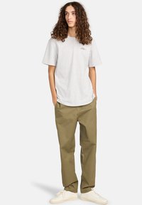 Lys grå kortærmet t-shirt med rundet kant, sammen med olivengrønne, løstsiddende bukser og hvide sneakers.