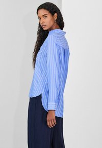 Blue and white striped shirt with long sleeves, a high-low hem, and a breast pocket. The fabric appears lightweight and smooth.