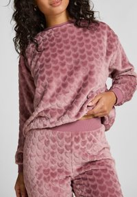 Zestaw dresowy w zakurzonym różu, wykonany z fakturowanej mikropolaru, z falistym wzorem. Posiada ściągacze przy mankietach i w pasie, zapewniając wygodny i swobodny krój.