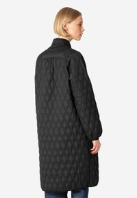Abrigo acolchado negro con collar alto, con patrones en forma de diamante, mangas largas y un corte holgado, que se extiende por debajo de las rodillas.