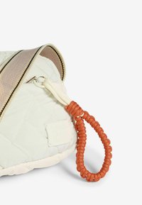 Borsa crema trapuntata con manico in paracord arancione, caratterizzata da una tracolla a righe contrastanti e un'etichetta testurizzata con la scritta "amici come questi".