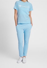 Jasnoniebieska bawełniana koszulka z okrągłym dekoltem i krótkimi rękawami, z białym logo. Połączona z pasującymi lekkimi spodniami dresowymi i białymi trampkami.