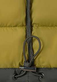 Elastische trekband met metalen sluiting op groen en grijs gewatteerd stof, waarschijnlijk onderdeel van een jas of buitenkleding.