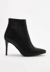 Bottine en cuir noir avec un bout pointu, une texture lisse et un talon haut et fin. Couture minimale et design épuré.