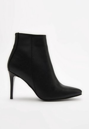 Bota de tobillo de cuero negro con punta puntiaguda, textura lisa y tacón alto y delgado. Costuras mínimas y diseño elegante.