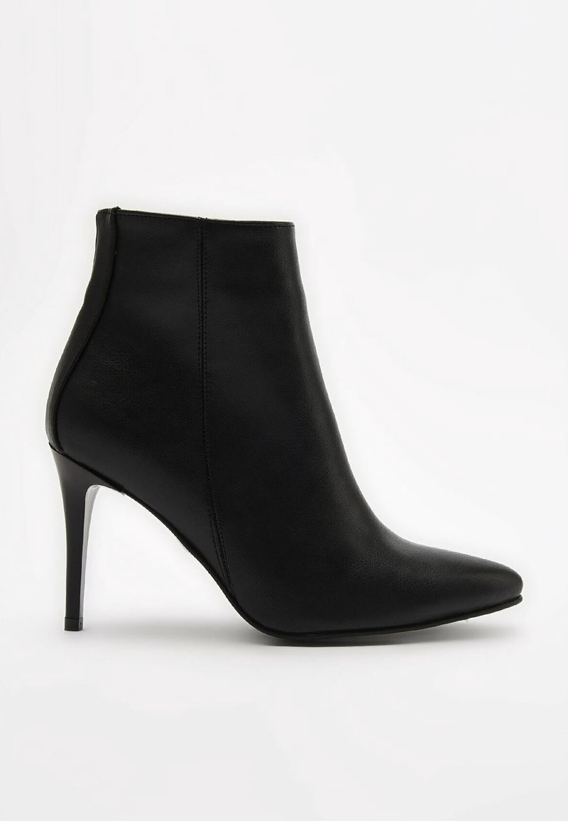 Bottine en cuir noir avec un bout pointu, une texture lisse et un talon haut et fin. Couture minimale et design épuré.