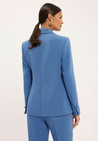 Niebieski żakiet o dopasowanym kroju, wykonany z gładkiego materiału, z klapami, mankietami na guziki i eleganckim, dopasowanym fasonem z rozcięciem z tyłu.